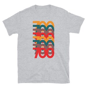 Puede incluir: Una camiseta gris jaspeada con un gr&aacute;fico retro del n&uacute;mero 700 en capas superpuestas de rojo, naranja, amarillo, verde y marr&oacute;n.