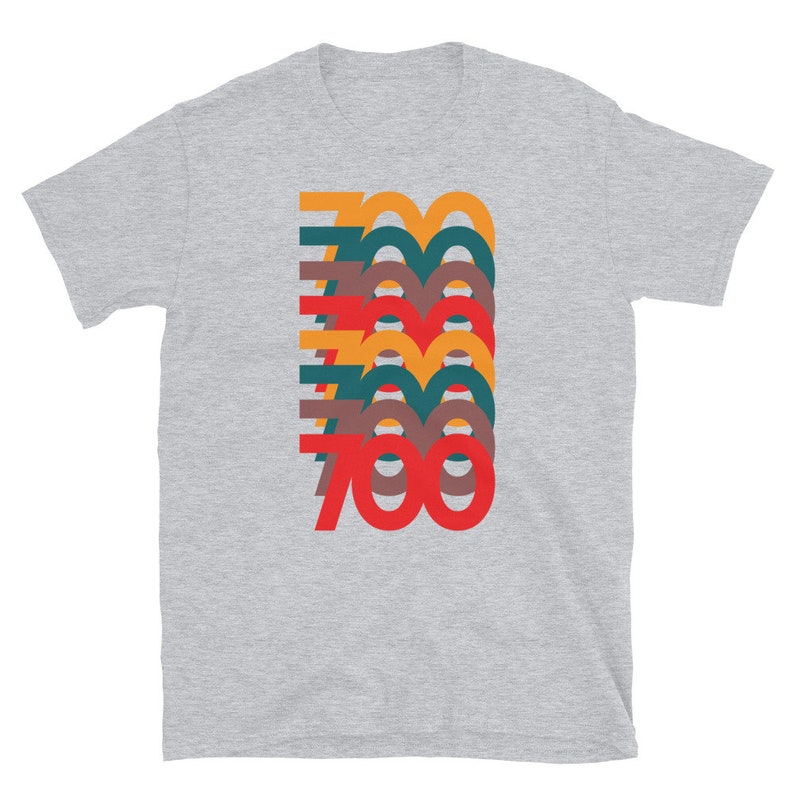 Puede incluir: Una camiseta gris jaspeada con un gr&aacute;fico retro del n&uacute;mero 700 en capas superpuestas de rojo, naranja, amarillo, verde y marr&oacute;n.