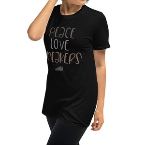 May include: Black t-shirt with the text "Peace Love Sneakers" in a light brown color.