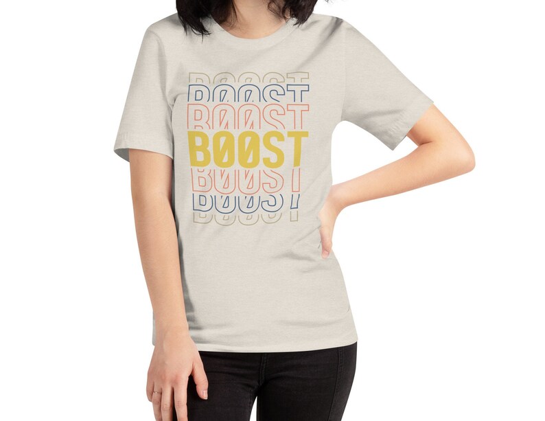 May include: A light beige t-shirt with a graphic print of the word "BOOST" in yellow, with the word "BOOST" repeated in different colors above and below the main word.