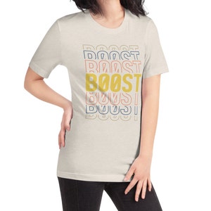 May include: A light beige t-shirt with the word "BOOST" printed in yellow, red, and blue. The word is repeated multiple times, with each repetition slightly offset from the one above it.
