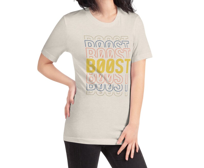 May include: A light beige t-shirt with the word "BOOST" printed in yellow, red, and blue. The word is repeated multiple times, with each repetition slightly offset from the one above it.
