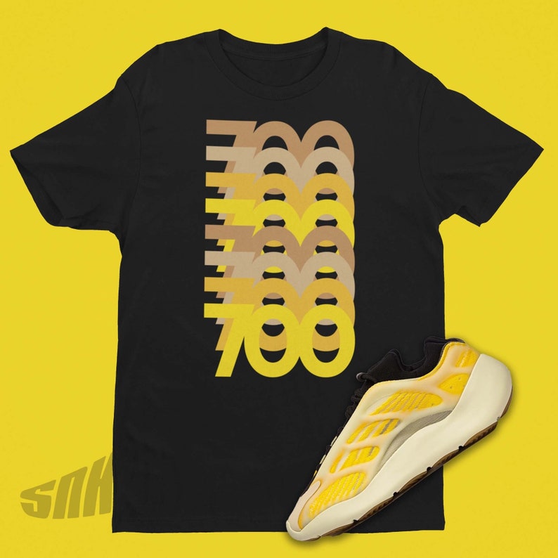 May include: Black t-shirt with a graphic of the number 700 repeated in different shades of yellow and brown. A yellow and white sneaker with a black accent is shown in the bottom right corner of the image.