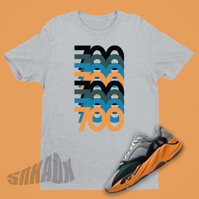 Peut inclure: Un t-shirt gris avec le nombre 700 r&eacute;p&eacute;t&eacute; dans un design empil&eacute; dans des tons de bleu, vert et orange. Une paire de baskets grises, vertes et orange avec un motif de flamme sur la semelle.