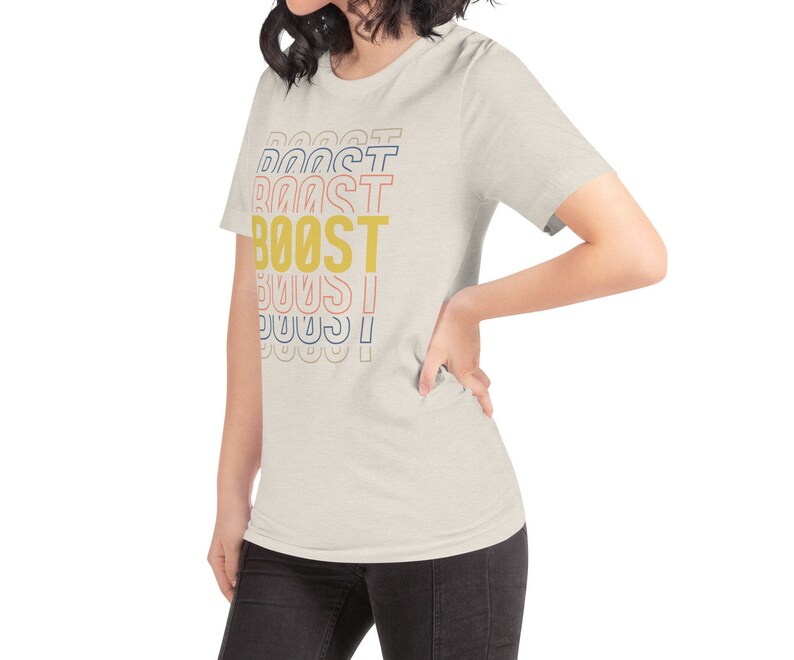 May include: A light beige t-shirt with the word "BOOST" printed in yellow, red, blue, and pink letters. The letters are stacked on top of each other, with the word "BOOST" in the center.