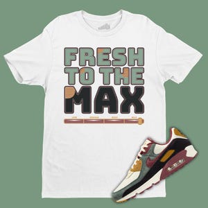 May include: White t-shirt with the text "Fresh to the Max" in black and green lettering. A graphic of a progress bar with the words "Low", "Medium", "High", and "Max" is below the text. A pair of brown, green, and black sneakers are in the bottom right corner of the image.