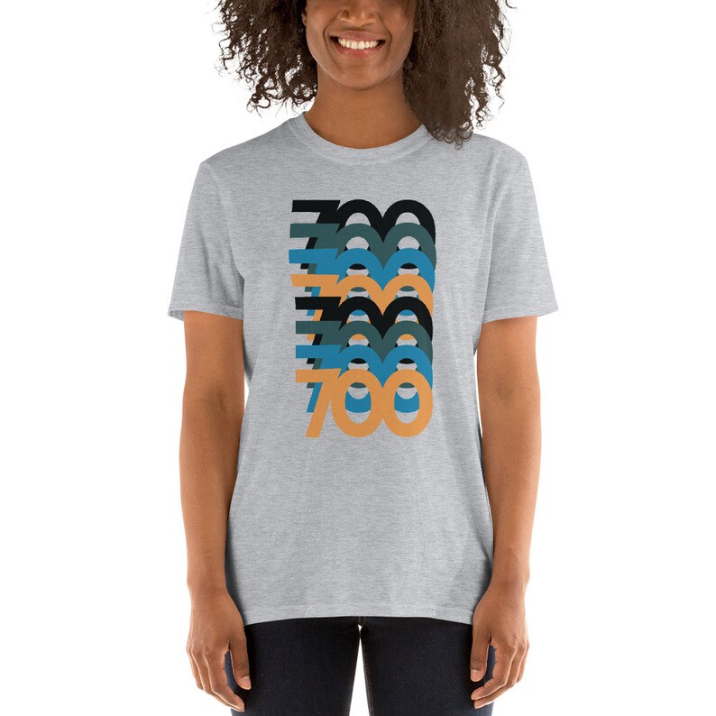 Peut inclure: Un t-shirt gris chin&eacute; avec un motif graphique repr&eacute;sentant le nombre 700 r&eacute;p&eacute;t&eacute; dans diff&eacute;rentes couleurs, notamment le noir, le bleu sarcelle et l'orange.