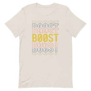 May include: A beige t-shirt with a graphic design of the word "BOOST" in yellow, with the word "BOOST" repeated in different colors and sizes above and below the main word.
