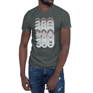 May include: A dark heather grey t-shirt with a graphic design of the number 386 repeated in a layered, overlapping pattern. The numbers are in shades of grey and white.
