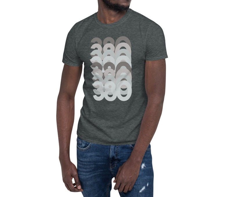 May include: A dark heather grey t-shirt with a graphic design of the number 386 repeated in a layered, overlapping pattern. The numbers are in shades of grey and white.