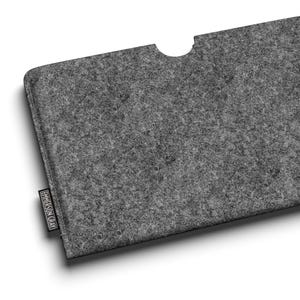 May include: A grey felt tablet sleeve with a curved top cutout. A black elastic band is attached to the right side. The brand name "EMERSON GRAY" is printed on a small tag on the lower left corner. The sleeve is designed to hold a tablet.