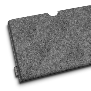 May include: A gray felt laptop sleeve with a curved cutout at the top. The sleeve has a rectangular shape and a textured surface. A small black label is attached to the bottom left corner.