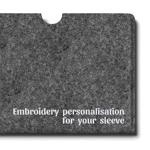 Könnte beinhalten: Eine dunkelgraue Laptophülle aus Filz mit einem halbkreisförmigen Ausschnitt in der oberen Mitte. Der Text "Embroidery personalisation for your sleeve" ist unten rechts in Weiß aufgedruckt, ein kleines schwarzes Etikett zeigt "EMMERSON CRAY".