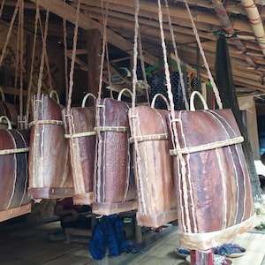 Puede incluir: Una colección de bolsas tejidas marrones que cuelgan del techo. Las bolsas están hechas de materiales naturales y tienen un aspecto rústico. Están suspendidas de una estructura de madera con cuerda.