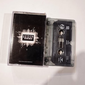 May include: A cassette tape with a black and white cover featuring the band name "TOOL" and album title "ÆNIMA". The cassette is in a clear plastic case. The text "HANYA UNTUK DIJUAL DI INDONESIA" is visible.