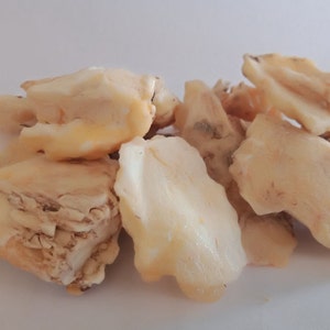 May include: Close-up of a pile of pale yellow and white resin pieces. The resin is translucent and has a slightly rough texture.