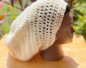 Puede incluir: Un gorro blanco de punto de ganchillo con una trama suelta y abierta. El gorro se lleva en una cabeza de maniquí.
