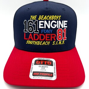 May include: A navy blue and red baseball cap with the text "THE BEACHBOYS 161 ENGINE 81 LADDER SOUTHBEACH S.I.N.Y." The cap has a red brim and a small red button on top. The cap has a "OTTO" label.