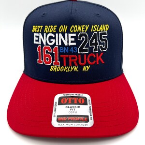 May include: A navy blue baseball cap with a red brim and a red button on top. The front features embroidered text: BEST RIDE ON CONEY ISLAND, ENGINE 245, 161 TRUCK, BN 43, and BROOKLYN, NY. A sticker on the brim reads OTTO PREMIUM FABRIC CLASSIC FIT.