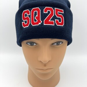 May include: Navy blue knit beanie with the embroidered text "SQ 25" in red with a white outline. The beanie is displayed on a mannequin head.