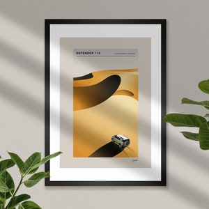 May include: A framed print of a Land Rover Defender 110 driving through sand dunes in the Kalahari Desert, Botswana. The print is in a black frame with a white mount.
