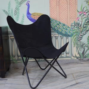 May include: Black butterfly chair with a metal frame. The chair has a distinctive, curved silhouette and a fabric seat. The chair is set against a backdrop of a colorful mural featuring a peacock and floral elements.