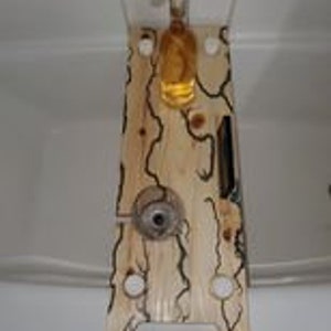 Puede incluir: Un botellero de madera con una botella de vino y una copa. El botellero tiene un acabado de veta de madera natural con detalles oscuros en forma de vid. Cuenta con cortes circulares y un asa en la parte inferior.