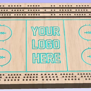 Può includere: Un tabellone di cribbage in legno con un design di pista di hockey. Il tabellone ha tre file di buchi e le parole "YOUR LOGO HERE" al centro.