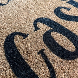 May include: Close-up of a brown coir doormat with the words "Welcome" in black lettering.