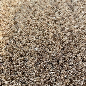 May include: Close-up of a brown coir doormat with a textured surface. The fibers are tightly woven and create a dense, durable surface.