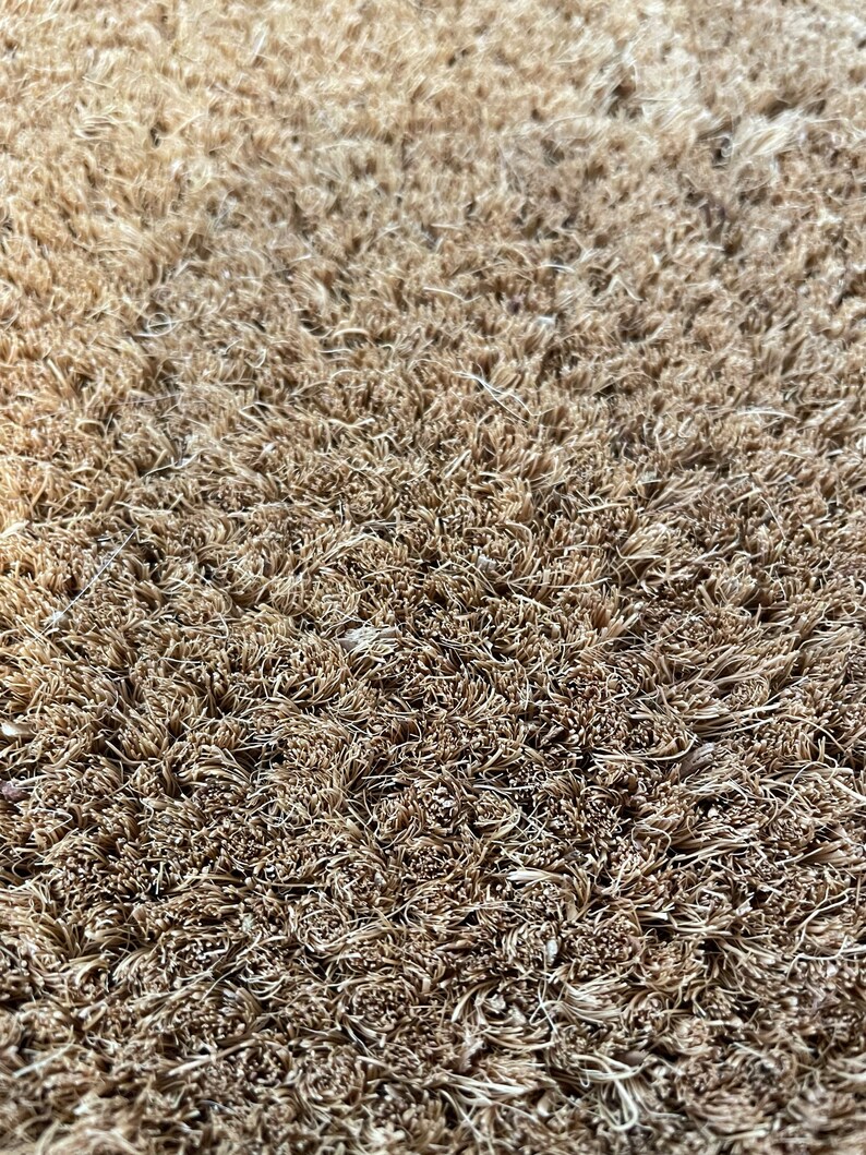 May include: Close-up of a brown coir doormat with a textured surface. The fibers are tightly woven and create a dense, durable surface.