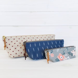 Op de afbeelding: Drie stoffen ritszakjes in verschillende maten en patronen. Het grootste zakje is rood met witte stippen, het middelste zakje is blauw met een wit bladpatroon en het kleinste zakje is grijs met een roze en groen bloemenpatroon.