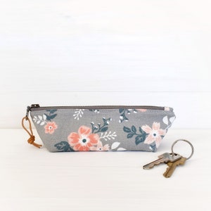 Op de afbeelding: Een grijze ritszak met een bloemenprint met roze bloemen en groene bladeren. De tas heeft een bruin leren bandje.