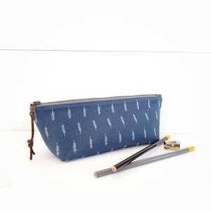 Op de afbeelding: Een blauwe potlood etui met een wit blad patroon en een bruine leren rits. Twee potloden en een puntenslijper liggen naast de etui.