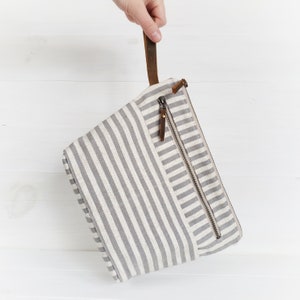 May include: A gray and white striped canvas zippered pouch with a brown leather handle.