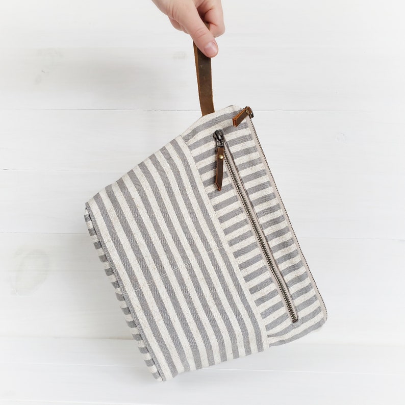 May include: A gray and white striped canvas zippered pouch with a brown leather handle.