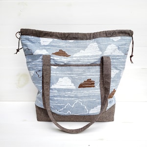 May include: A brown and blue tote bag with a cloud pattern. The bag has brown straps and a drawstring closure.