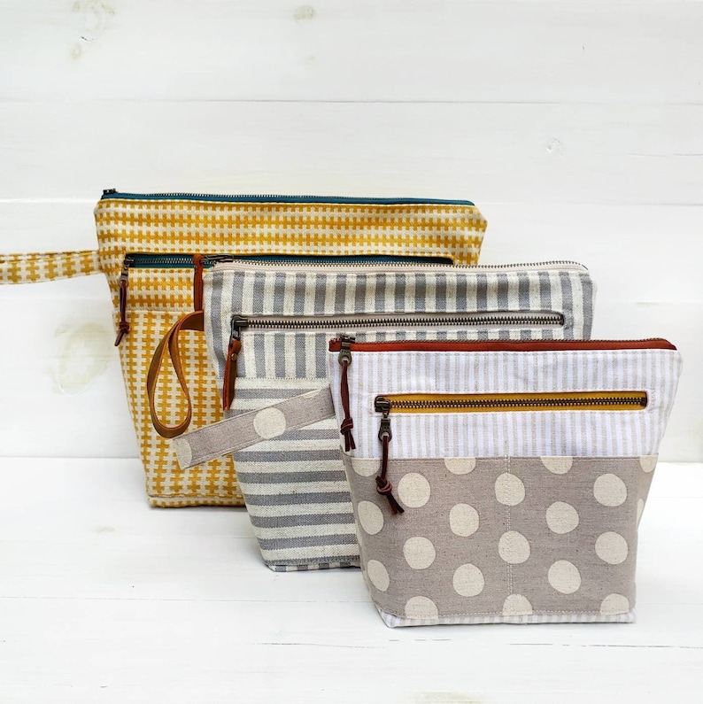 May include: Three zippered pouches in different patterns. The top pouch is yellow with a checkered pattern. The middle pouch is gray and white with a striped pattern. The bottom pouch is gray with white polka dots.