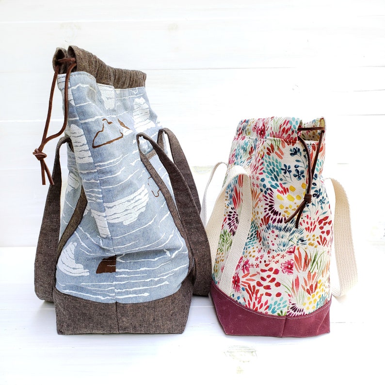 May include: Two tote bags, one with a blue and white striped pattern and the other with a colorful floral pattern. Both bags have brown leather handles and are made of fabric.