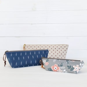 Op de afbeelding: Drie ritszakjes met verschillende patronen. Het zakje bovenaan is bruin met witte stippen. Het middelste zakje is blauw met witte takjes. Het onderste zakje is grijs met roze bloemen.