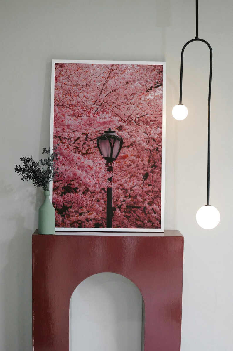 Puede incluir: Una impresi&oacute;n enmarcada de una farola bajo una copa de cerezos en flor rosa. La impresi&oacute;n est&aacute; colgada en una pared sobre una consola arqueada de color burdeos.