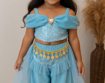 May include: A light blue princess costume for a child. The outfit includes a sequined crop top with off-the-shoulder sleeves, matching harem pants with bows, and a gold coin belt. A blue headband with a jewel completes the look.