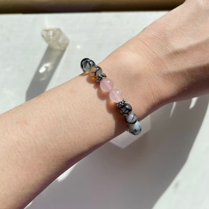 May include: A beaded bracelet featuring a combination of rose quartz and patterned agate beads. The bracelet is accented with silver-colored spacers. The bracelet is worn on a wrist.