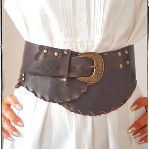 May include: A brown leather belt with a large, ornate brass buckle. The belt has decorative stitching and metal studs.
