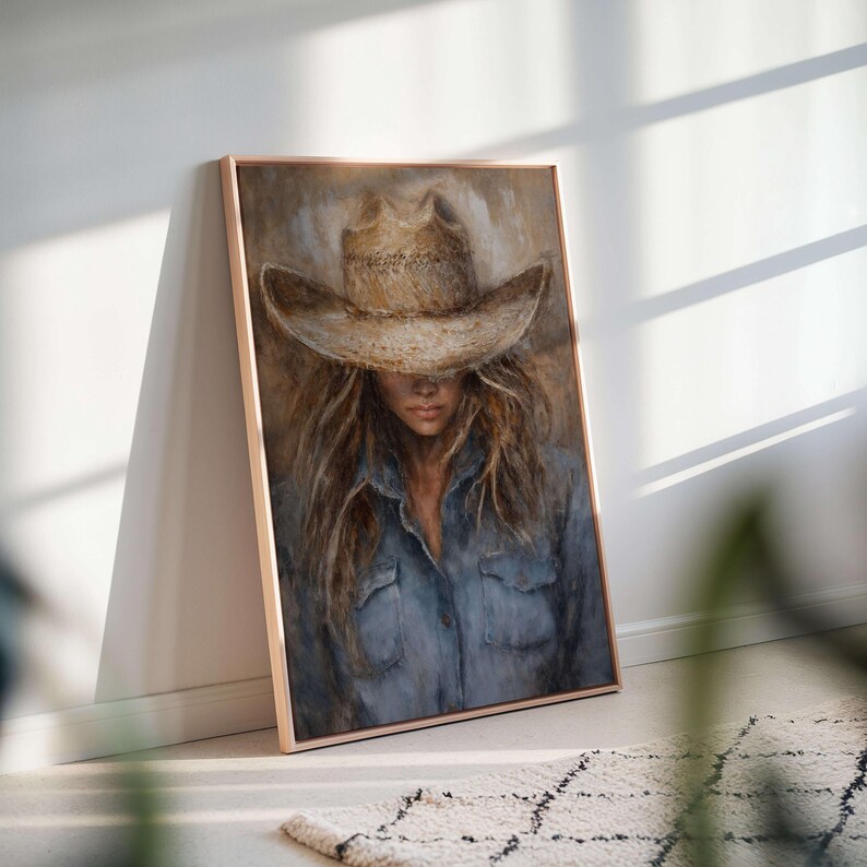 May include: A framed portrait of a person wearing a cowboy hat and a denim shirt. The artwork features a neutral color palette with shades of brown, beige, and blue. The person's face is partially obscured by the hat, creating a sense of mystery.