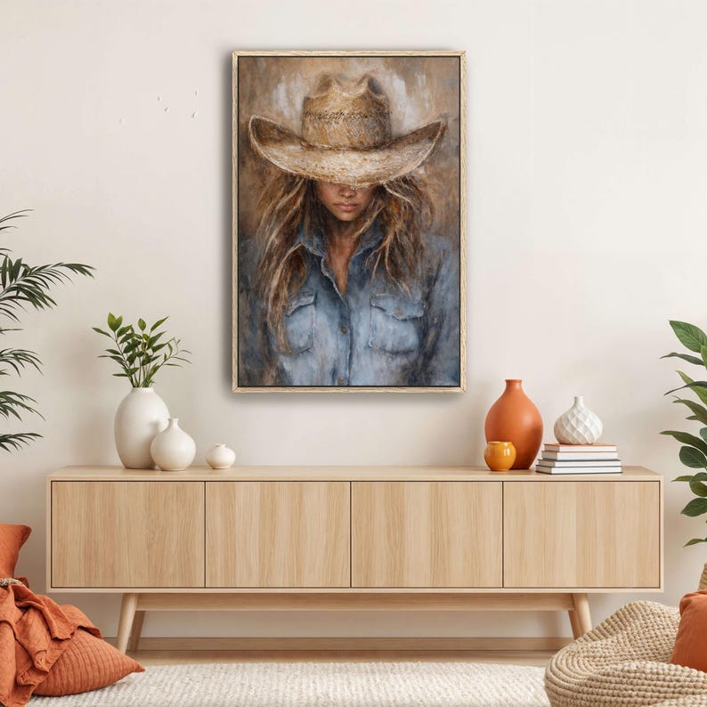 May include: A framed painting depicts a person wearing a straw cowboy hat and a blue denim shirt. The artwork has a neutral color palette with shades of brown, beige, and blue. The person's face is partially obscured by the hat, creating a sense of mystery.