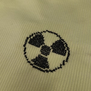 Puede incluir: Primer plano de una tela verde claro con un símbolo de radiación bordado en negro.