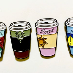 以下が含まれることがあります： 異なるキャラクターの名前とデザインが施されたコーヒーカップの形をしたエナメルピン5個セット。カップは青、緑、ピンク、赤、水色です。カップに書かれている名前は「サリー」、「ブライドローズ」、「ラプンツェル」、「オーロラ」、「ベル」です。