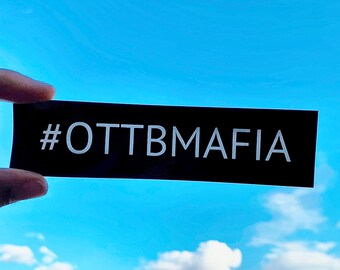 May include: A black rectangular sticker with white text that reads "#OTTBMAFIA" against a blue sky with white clouds.