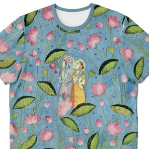 May include: A light blue t-shirt featuring a detailed illustration of a couple surrounded by pink lotus flowers and green lily pads. The shirt has a crew neck and a repeating pattern of the floral design.